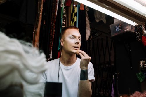 Free A drag queen applies makeup in a vibrant dressing room filled with costumes. Stock Photo