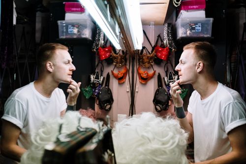 Free A man preparing for a performance by applying makeup in a dressing room mirror. Stock Photo