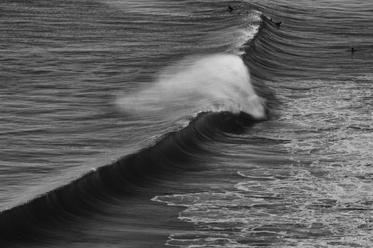 Black and white photo of waves at Arraial do Cabo beach, capturing surfers and ocean motion.