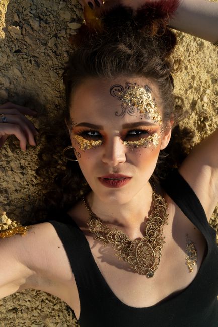 From above of attractive woman with bright eyes and makeup and transfer tattoos lying on dry ground