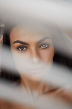 A stunning portrait of a young woman shot through blinds in natural light, capturing her captivating gaze.