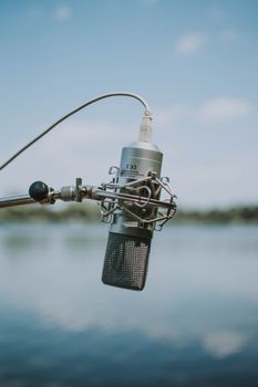 Professional microphone mounted into stand on blurred background of nature on sunny day