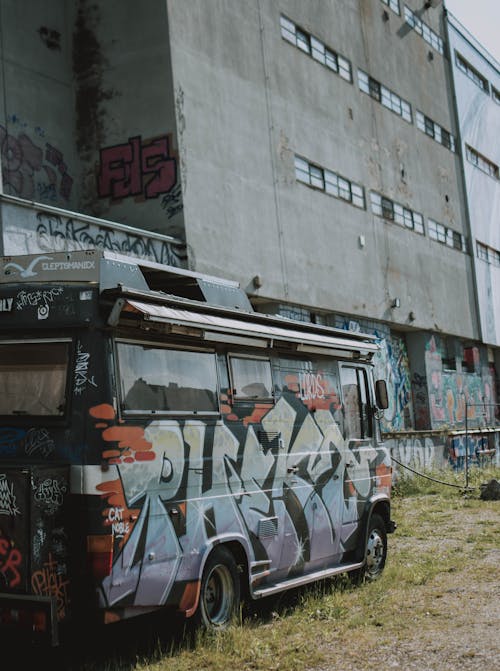 Van in bright paint parked near old shabby stone building with careless inscriptions