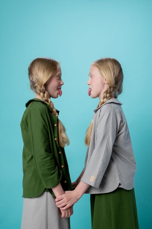 Free Blonde twin sisters holding hands and sticking tongues out against a turquoise backdrop. Stock Photo