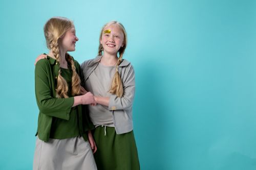Free Twin blond girls with braids smiling and embracing against a turquoise background, indoors. Stock Photo