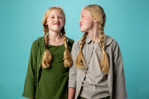 Free Playful twin sisters with blonde braids having fun against a turquoise background indoors. Stock Photo
