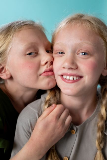 Close-up of twin girls smiling with a turquoise background, showcasing youthful joy.