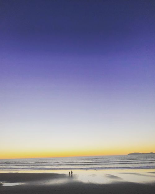 Free Peaceful beach scene at sunset in Rosarito, Mexico with two silhouettes by the water. Stock Photo