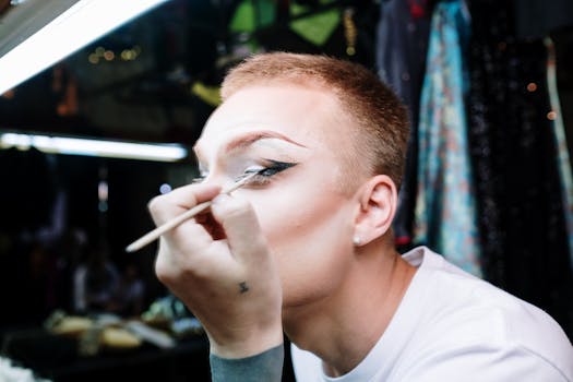 A drag queen applies eye makeup in a dressing room, getting ready for a performance.