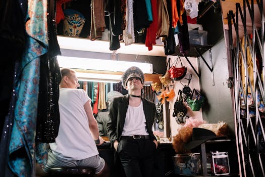 Two performers prepare in a theatrical dressing room, featuring costumes and vibrant attire.