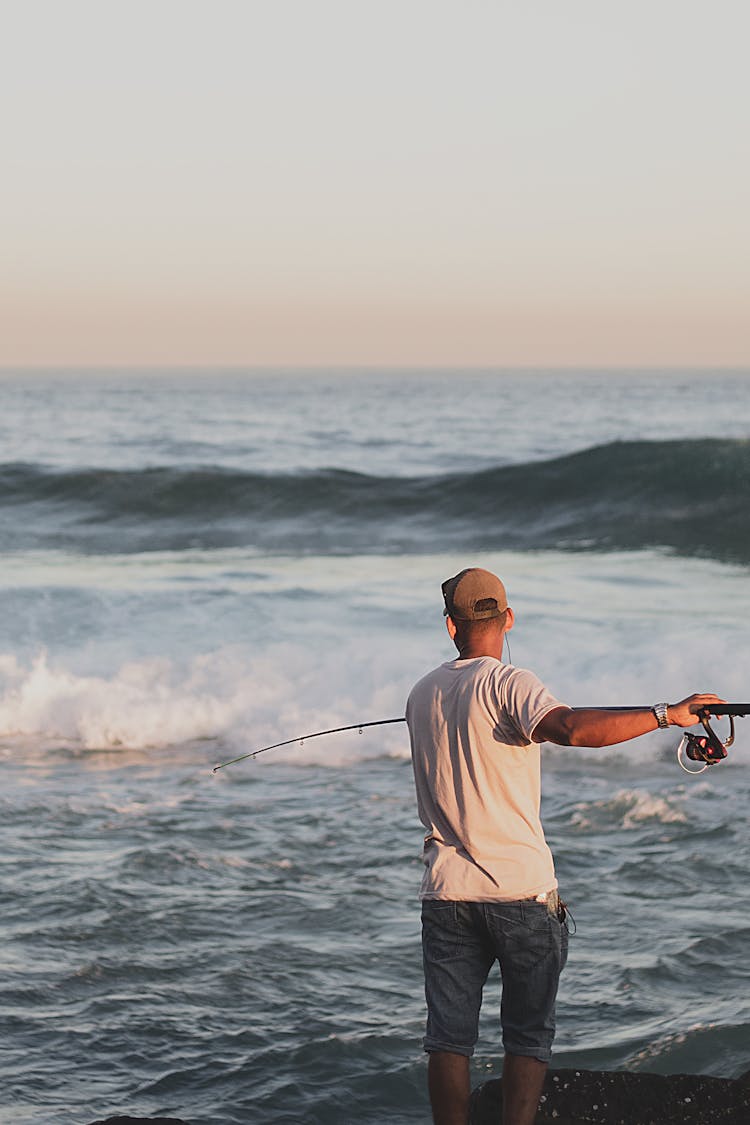 Anonymous Fisherman Catching Fish On Ocean In Evening