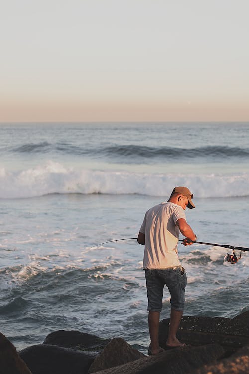 Anonymous fisherman fishing on stormy sea standing on stones