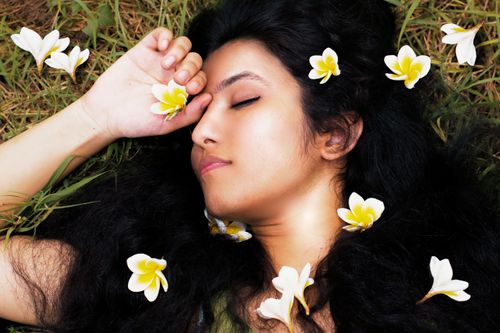 Free A peaceful woman with closed eyes lies on grass surrounded by white frangipani flowers. Stock Photo