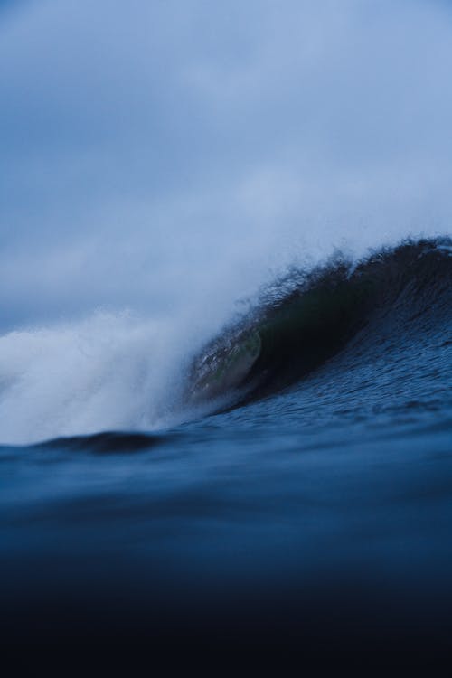 Foamy powerful wave rolling in stormy ocean under gray cloudy sky in daytime