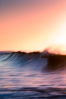 Spectacular majestic waves of powerful ocean under cloudless sky in bright orange sunset