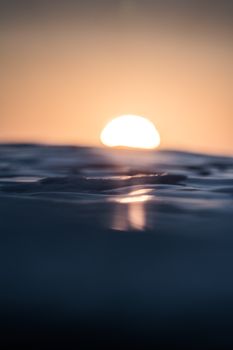 Glistening ripples in dark water on blurred background of downing sun in orange sky