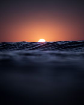 Shiny orange sun over rippling wavy water of vast sea in bright sunset in evening