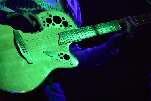 A close-up view of an acoustic guitar being played by a musician under green stage lights.