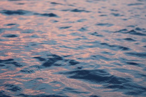 Free A calming view of ocean waves reflecting the warm hues of a setting sun, creating a peaceful ambiance. Stock Photo