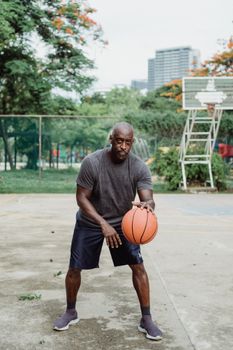 A man dribbling a basketball on an outdoor court in an urban park setting.