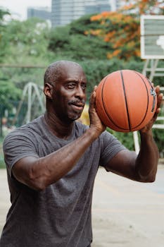 Senior adult African American man focusing on shooting a basketball at an outdoor court.
