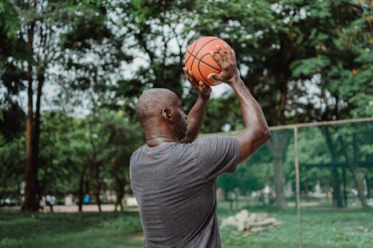 Back view of a man holding a basketball, ready to shoot on an outdoor court surrounded by greenery.