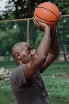 Man practicing basketball shot outdoors on a summer day.