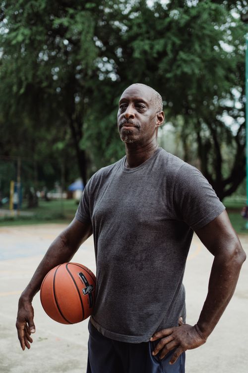 Free African American man standing with a basketball on an outdoor court, ready for the game. Stock Photo