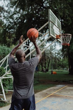 Man playing basketball in a park, aiming a shot towards the hoop.