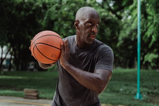 Middle-aged man in gray shirt playing basketball outdoors, displaying focus and determination.