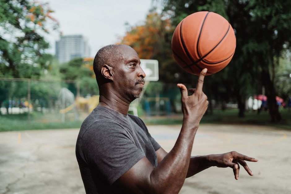 A focused black male basketball player skillfully balances a basketball on his finger outdoors. A focused black male basketball player skillfully balances a basketball on his finger outdoors.