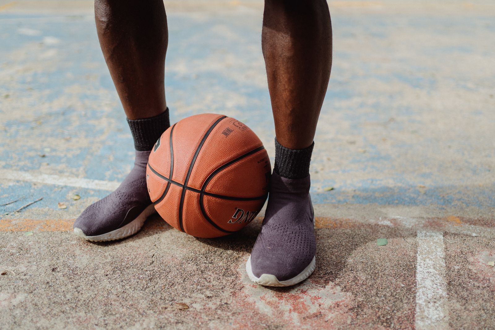 Basketball player lower legs, shoes, ankle area, and ball on an outdoor court for basketball ankle brace selection. Photo: Pexels.