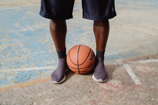 Close-up of a person standing with a basketball on an outdoor court, wearing shorts and sneakers.