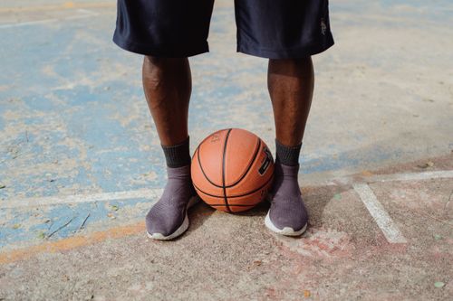Free Close-up of a person standing with a basketball on an outdoor court, wearing shorts and sneakers. Stock Photo