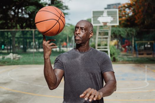 Athletic man with beard skillfully spinning a basketball on an outdoor court.