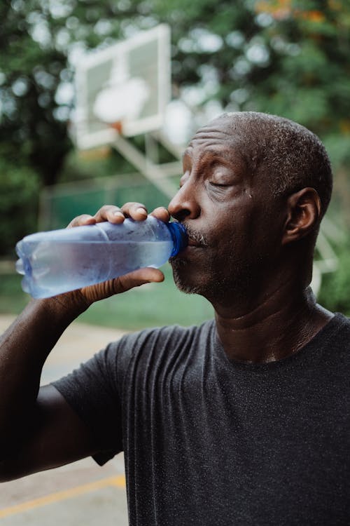 Free Man in Black Crew Neck Shirt Drinking Water from Blue Plastic Bottle Stock Photo
