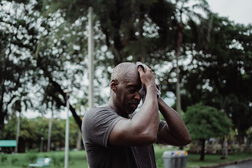 Shallow Focus Photo of Man in Gray Shirt Wiping His Face With Face Towel