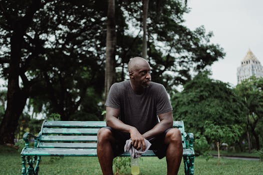 锻炼结束后，男子坐在公园长凳上休息，手里拿着毛巾和瓶子