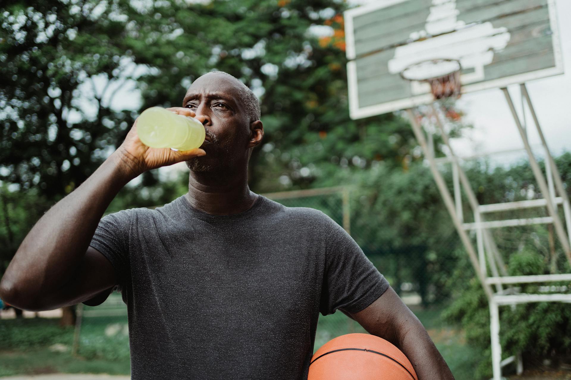 Man hydrates with sports drink on basketball court outdoors.