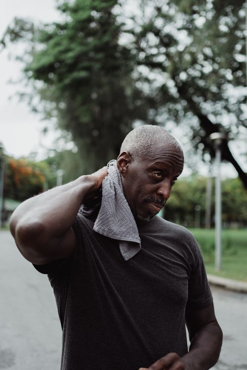 Free A man wipes his neck with a towel outdoors after an exercise session, looking focused. Stock Photo