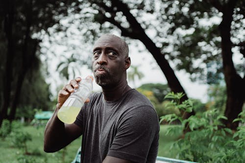 Man in Black Crew Neck T-shirt Drinking Yellow Liquid from Plastic Bottle