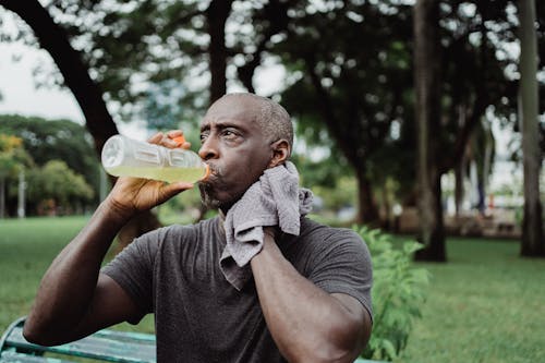 Man in Black Crew Neck T-shirt Drinking Yellow Liquid from Plastic Bottle