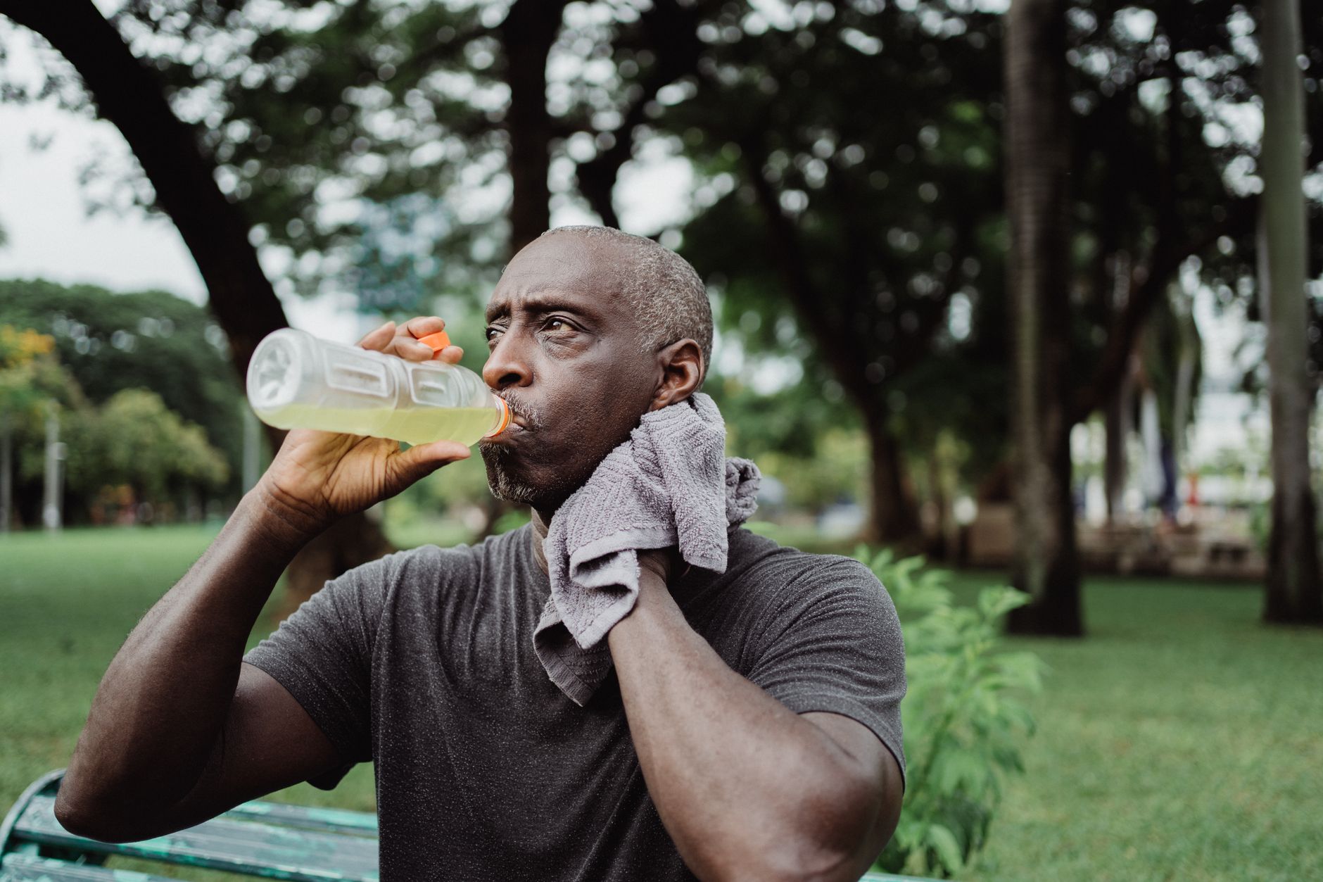football defender drinking an electrolyte bottle beside the pitch during a bright, humid afternoon training session