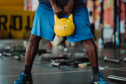 A fit black man performing a kettlebell lift in a gym setting, showcasing strength and fitness.