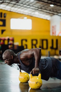 Strong man performing push-ups with kettlebells at a gym, showcasing fitness and determination.