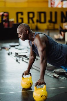 An athletic man performs a powerful kettlebell push-up in a gym, showcasing strength and determination.