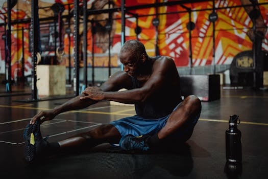 A man in a gym stretching on the floor, focusing on fitness and flexibility.
