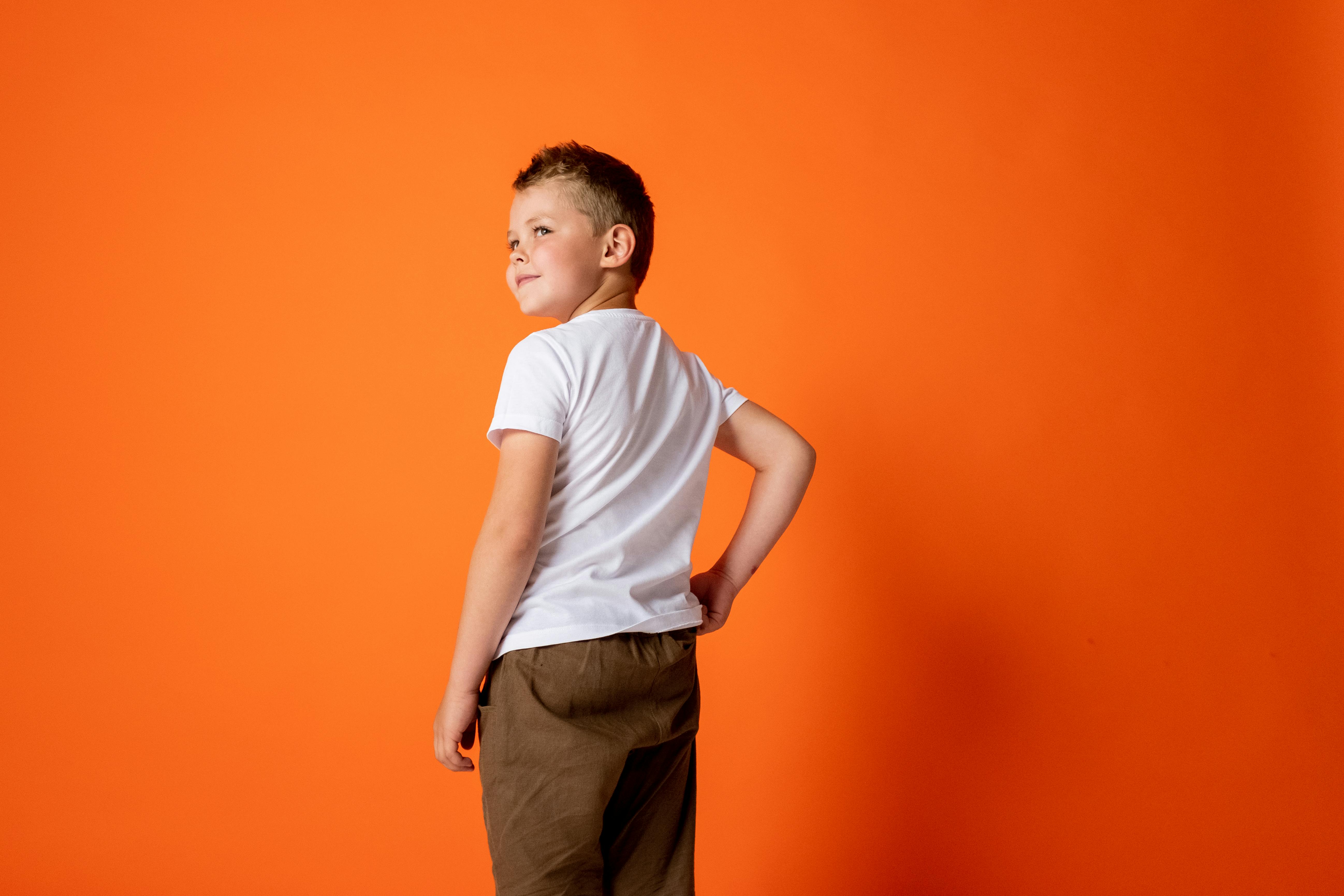 Boy in White Crew Neck T-shirt and Brown Pants Against Orange Background