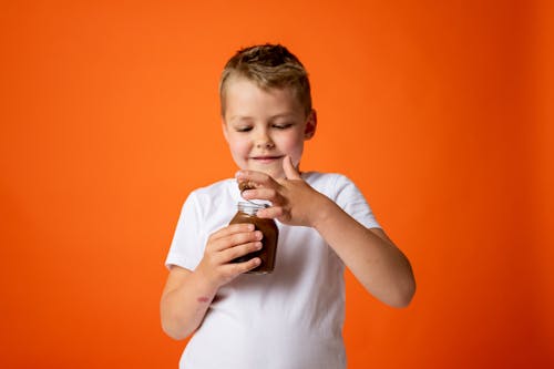 Мальчик в белой футболке с круглым вырезом держит банку с шоколадом
