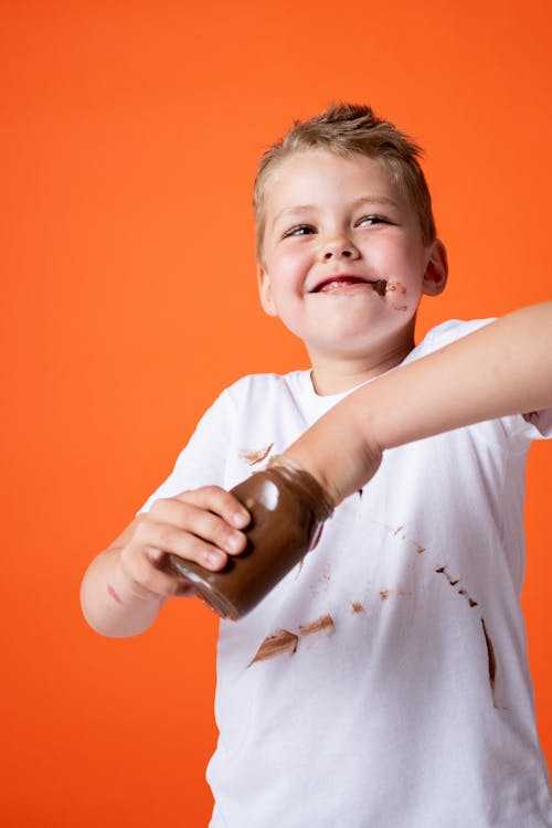 Boy in White Crew Neck T-shirt Holding Chocolate Jar